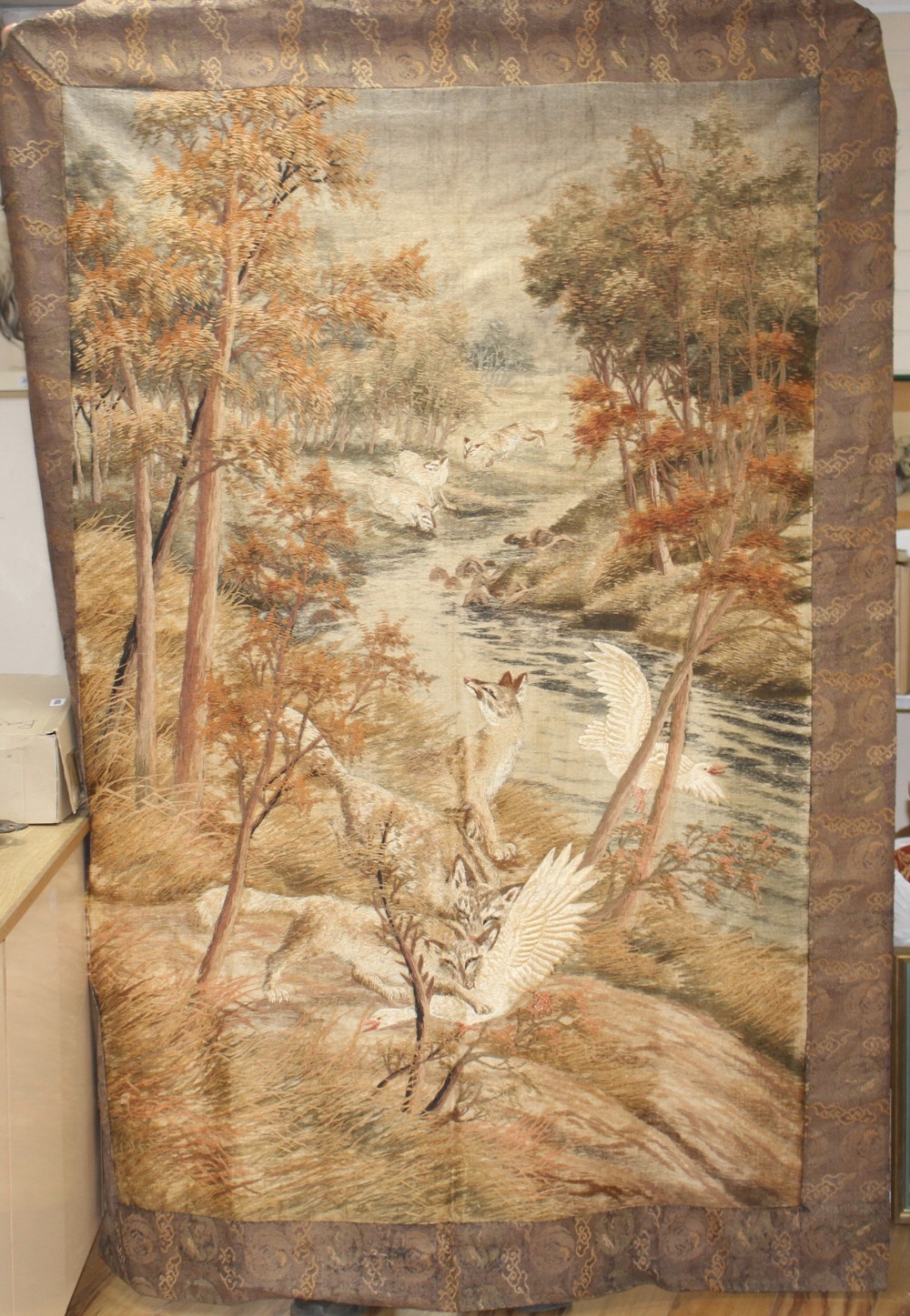 A 20th century Japanese silk panel, depicting wolves hunting geese beside a woodland stream, the inner panel 173 x 115cm, overall 205 x